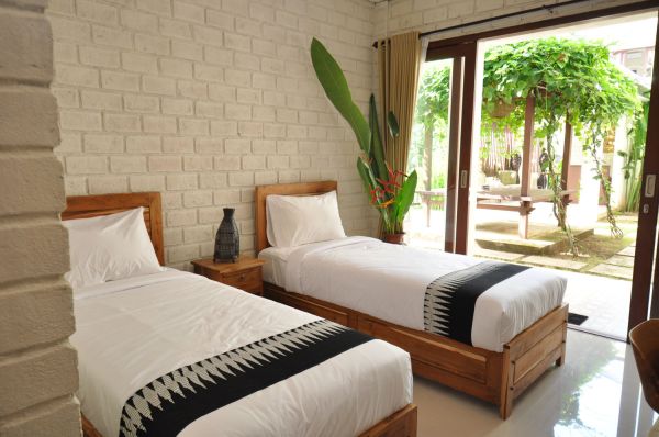 Cozy tropical bedroom with twin wooden beds, white linens, potted plants, and sliding doors to lush garden.